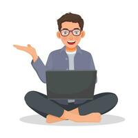 Young man with glasses using laptop computer while sitting on a floor showing hand for copy space vector