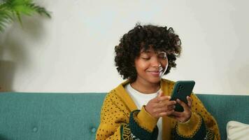 afrikanisch Mädchen halten Smartphone berühren Bildschirm Tippen scrollen Seite beim heim. Frau mit Zelle Telefon Surfen Internet mit Sozial Medien Apps spielen Spiel. Einkaufen online Internet Nachrichten Handy Sucht video