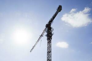 Tower building crane against the blue sky and sun. Construction of a new house. Construction of new buildings with a crane. Tower crane photo