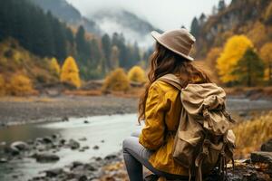 ai generado posterior ver de un elegante chica, con un mochila, un sombrero y un amarillo chaqueta, mirando a el ver de el montañas y el lago mientras relajante en el otoño naturaleza. viaje concepto. foto