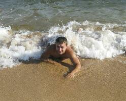 hombre en el apuntalar mentiras. el mar ola cubre el masculino. playa foto