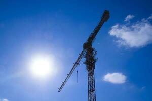 Tower building crane against the blue sky and sun. Construction of new buildings with a crane. Tower crane photo