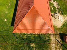 House with an orange roof made of metal, top view. Metallic profile painted corrugated on the roof. photo