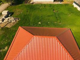 House with an orange roof made of metal, top view. Metallic profile painted corrugated on the roof. photo