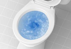 Top view of toilet bowl, blue detergent flushing in it photo