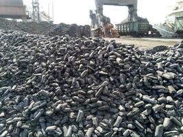 Piles of raw steel briquettes. Heap of coal anthracite in the port. Port cranes for coal loading photo