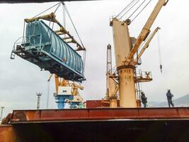 Moving freight railway car in the port by a port crane. Cargo lifting operations. Industrial port. photo