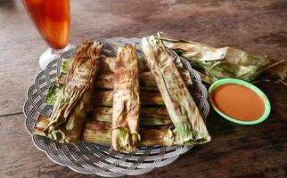 otak otak,grilled fish cakes wrapped with banana leaf.served with spicy sauce on wooden table photo