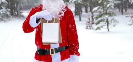 Santa Claus outdoor in winter and snow handing in hand eco paper bags with craft gift, food delivery. Shopping, packaging recycling, handmade, delivery for Christmas and New year photo