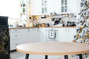 Round empty table to demonstrate the product with space for text in white kitchen, modern interior with a Christmas tree and fairy lights. New Year, Christmas mood, cozy home. photo