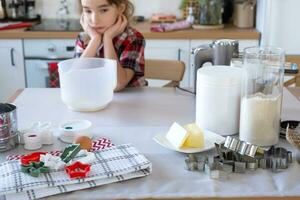 hija aprendizaje a cocinar ayuda en el blanco cocina amasar el masa en el cuenco para pan de jengibre y galletas para Navidad y nuevo año. niña trastornado y indeciso, triste foto