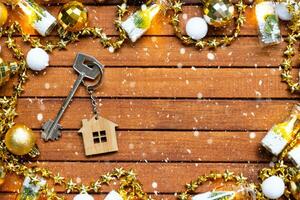 Key to house with a keychain tiny home on wooden background with Christmas decor layout. Gift for New Year, Christmas. Building, project, moving to new house, mortgage, rent and purchase real estate photo