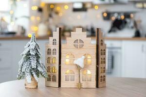 Key and tiny house of a small size on cozy home with Christmas decor on table of festive white kitchen. Gift for New Year. Insurance, moving to new house, mortgage, rent and purchase real estate photo