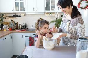 Mom and daughter in the white kitchen are preparing cookies, add ingredients. Family day, preparation for the holiday Christmas, learn to cook delicious pastries, cut shapes out of dough with molds photo