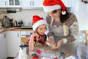 Mom and daughter in the white kitchen are preparing cookies for Christmas and new year. Family day, preparation for the holiday, learn to cook delicious pastries, cut shapes out of dough with molds photo