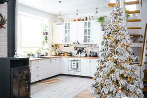 Festive Christmas decor in white kitchen, modern rustic interior with a snowy Christmas tree and fairy lights. New Year, Christmas mood, cozy home. The general plan photo