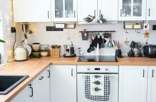 White Christmas decor in white kitchen, towel with Christmas trees, a branch of a fir tree on cabinets, induction cooker with oven. New Year, Christmas mood, cozy home. photo