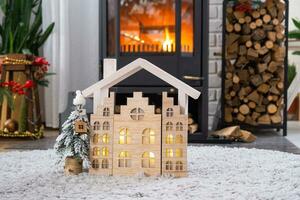 Key on Christmas tree and tiny house on cozy home with Christmas decor near the burning stove fireplace. Gift for New Year. Insurance, moving to new house, mortgage, rent and real estate photo