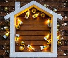 Tiny frame house on wooden background with Christmas decor layout and copy space. Gift for New Year, Christmas. Building, project, moving to new house, mortgage, rent and purchase real estate photo