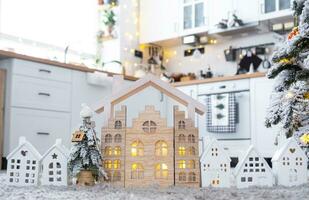 Key on Christmas tree and tiny house on cozy home with Christmas decor on table of festive white kitchen. Gift for New Year. Insurance, moving to new house, mortgage, rent and purchase real estate photo