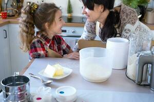 Mom and daughter in the white kitchen are preparing cookies, add ingredients. Family day, preparation for the holiday Christmas, learn to cook delicious pastries, cut shapes out of dough with molds photo