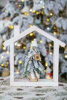 Key on Christmas tree and tiny house on cozy home with Christmas decor on table of festive white kitchen. Gift for New Year. Insurance, moving to new house, mortgage, rent and real estate photo