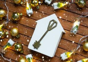 Key to house with a keychain tiny home on wooden background with Christmas decor layout. Gift for New Year, Christmas. Building, project, moving to new house, mortgage, rent and purchase real estate photo