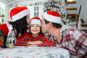 contento tradicional familia de papá, mamá, hija en festivo Papa Noel sombreros en un blanco cocina con un Navidad árbol y decoración. nuevo año, familia valores. foto