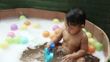 bambino avendo divertimento assunzione bagno giocando nel acqua con schiuma con colorato giocattoli. video