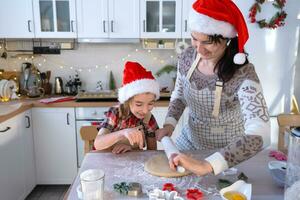 Mom and daughter in the white kitchen are preparing cookies for Christmas and new year. Family day, preparation for the holiday, learn to cook delicious pastries, cut shapes out of dough with molds photo