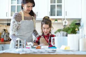 Mom and daughter in the white kitchen are preparing cookies, add ingredients. Family day, preparation for the holiday Christmas, learn to cook delicious pastries, cut shapes out of dough with molds photo