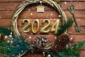 House key with keychain cottage on festive brown wooden background with stars, lights of garlands. New Year 2024 wooden letters, greeting card. Purchase, construction, relocation, mortgage, insurance photo