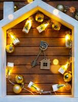 Key to house with a keychain tiny home on wooden background with Christmas decor layout. Gift for New Year, Christmas. Building, project, moving to new house, mortgage, rent and purchase real estate photo