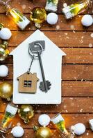 Key to house with a keychain tiny home on wooden background with Christmas decor layout. Gift for New Year, Christmas. Building, project, moving to new house, mortgage, rent and purchase real estate photo