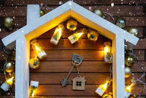 Key to house with a keychain tiny home on wooden background with Christmas decor layout. Gift for New Year, Christmas. Building, project, moving to new house, mortgage, rent and purchase real estate photo