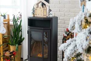 Metall black stove, burning hearth fireplace in white Festive interior of house is decorated for Christmas and New Year, Christmas tree. firewood in the woodpile, cozy and heating of home photo