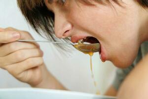 retrato de un adolescente comiendo sopa de remolacha con un cuchara. de cerca foto