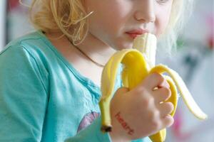 retrato de un pequeño niña comiendo un banana. el concepto de sano alimento. un Fresco rápido bocadillo foto