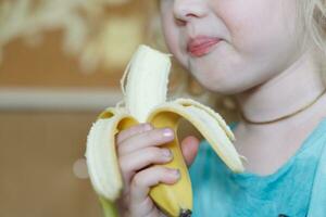 Portrait of a little girl eating a banana. The concept of healthy food. A fresh quick snack photo