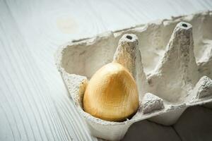 Golden egg in a regular cardboard egg tray. The concept of a rich life. photo