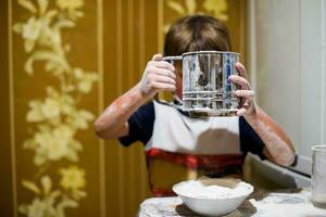 A little boy is playing with flour and milk in the kitchen. photo