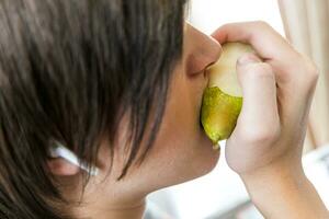 retrato de un Adolescente chico comiendo un pera. de cerca foto