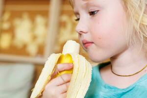 retrato de un pequeño niña comiendo un banana. el concepto de sano alimento. un Fresco rápido bocadillo foto