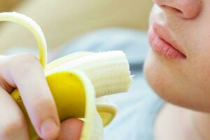 Portrait of a teenage boy eating a banana. Photo of a guy's mouth and lips with a banana. Fresh fruit. Healthy foods for children