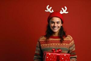 AI generated Portrait of a happy young woman in christmas sweater with reindeer horns holding present box isolated over red background photo