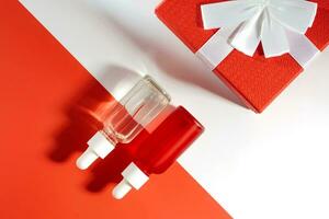 Two Bottles red and white with essential oils next to a red gift box with a bow. Gift for Valentine's Day, Christmas or mothers day. Body and hair care, mockup concept photo