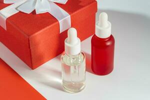 Cosmetic Dropper Bottles with Natural Self-Care Product next to red gift box. Present for holidays. Mockup photo