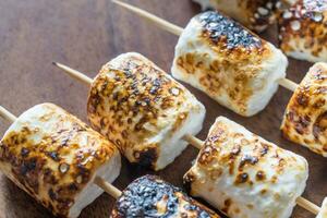 Marshmallow skewers on the wooden background photo