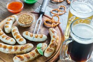 A la parrilla salchichas con pretzels y tazas de cerveza foto