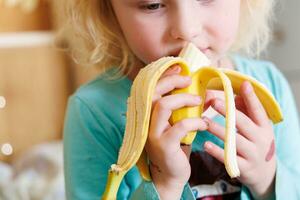 Portrait of a little girl eating a banana. The concept of healthy food. A fresh quick snack photo